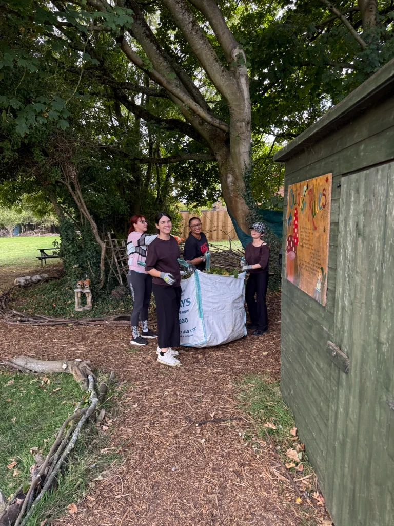 Four volunteers filling a large bag with cuttings under a tree
